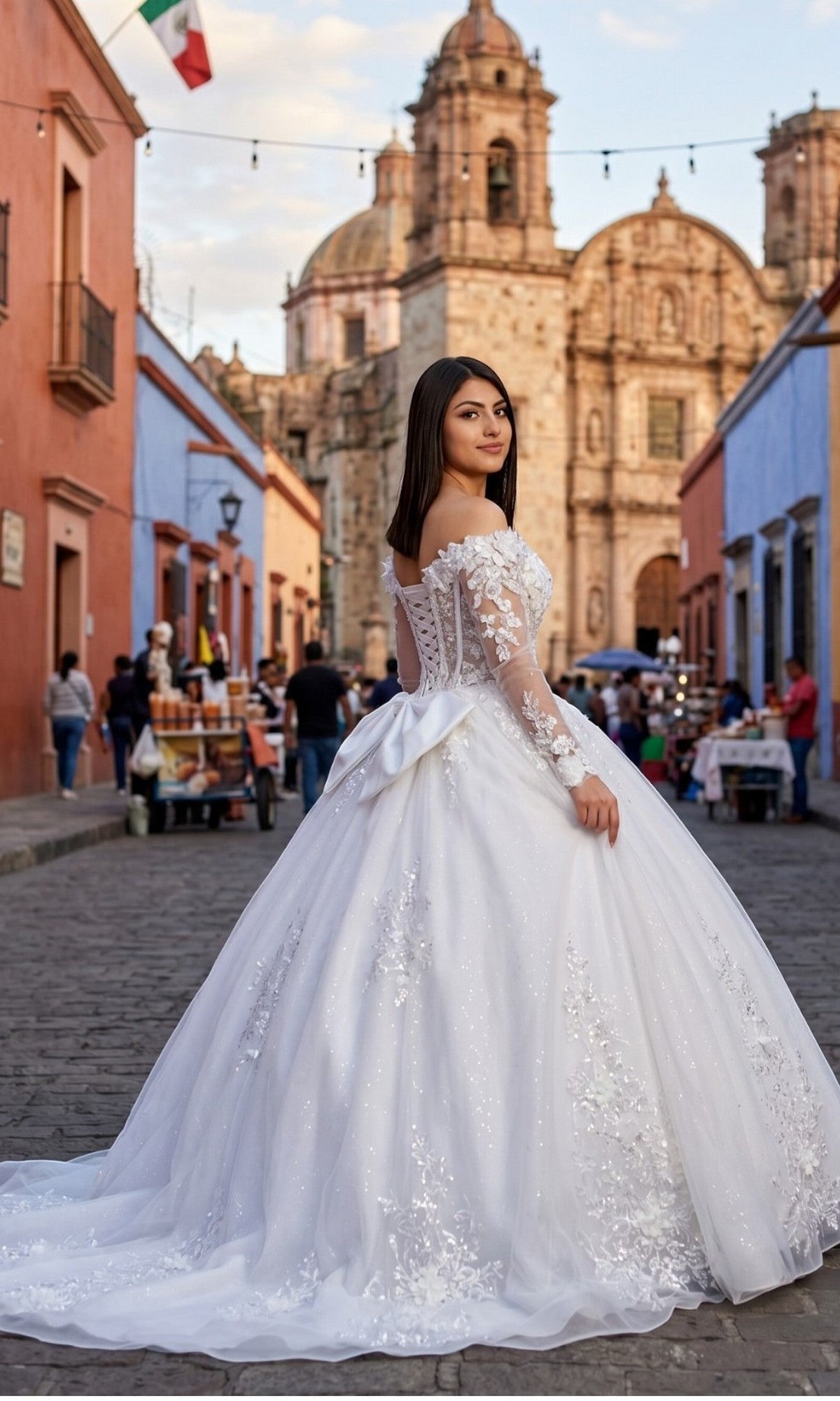 Wearing the Cinderella Couture 8325J long formal dress, a woman stands on a cobblestone street, framed by colorful buildings and a historic church in the background. The white gown features an off-the-shoulder neckline, a fitted corset bodice, and a glitter tulle ball gown skirt.